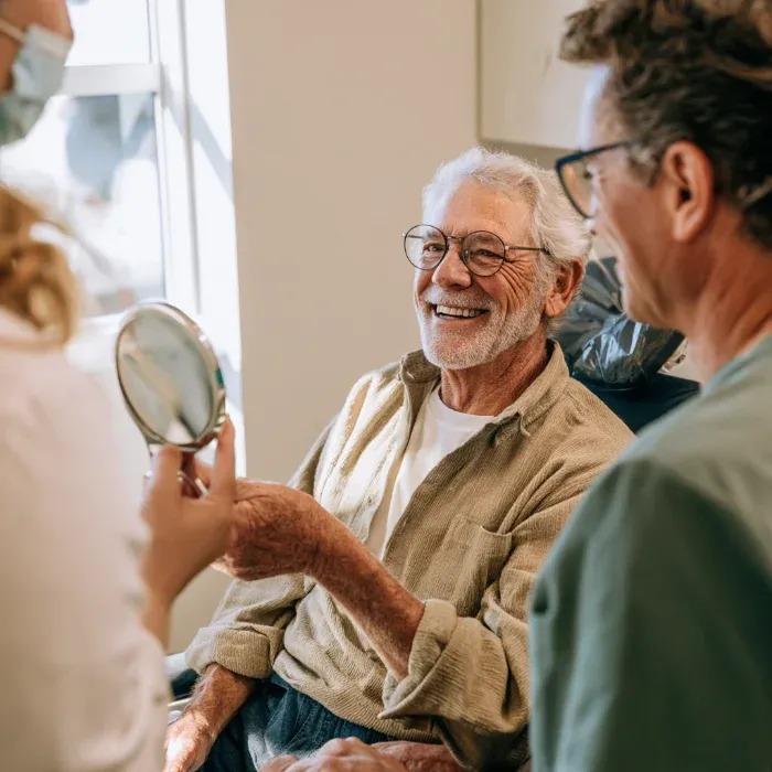 Smiling patient admiring his smile in a hand mirror